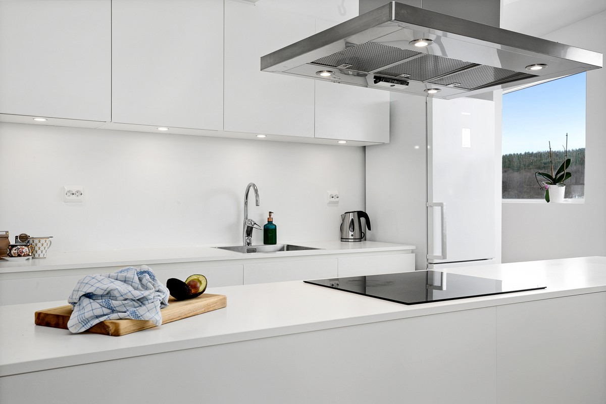 Kjøkken i moderne utførelse med stor kjøkkenøy, downlights og integrerte hvitevarer