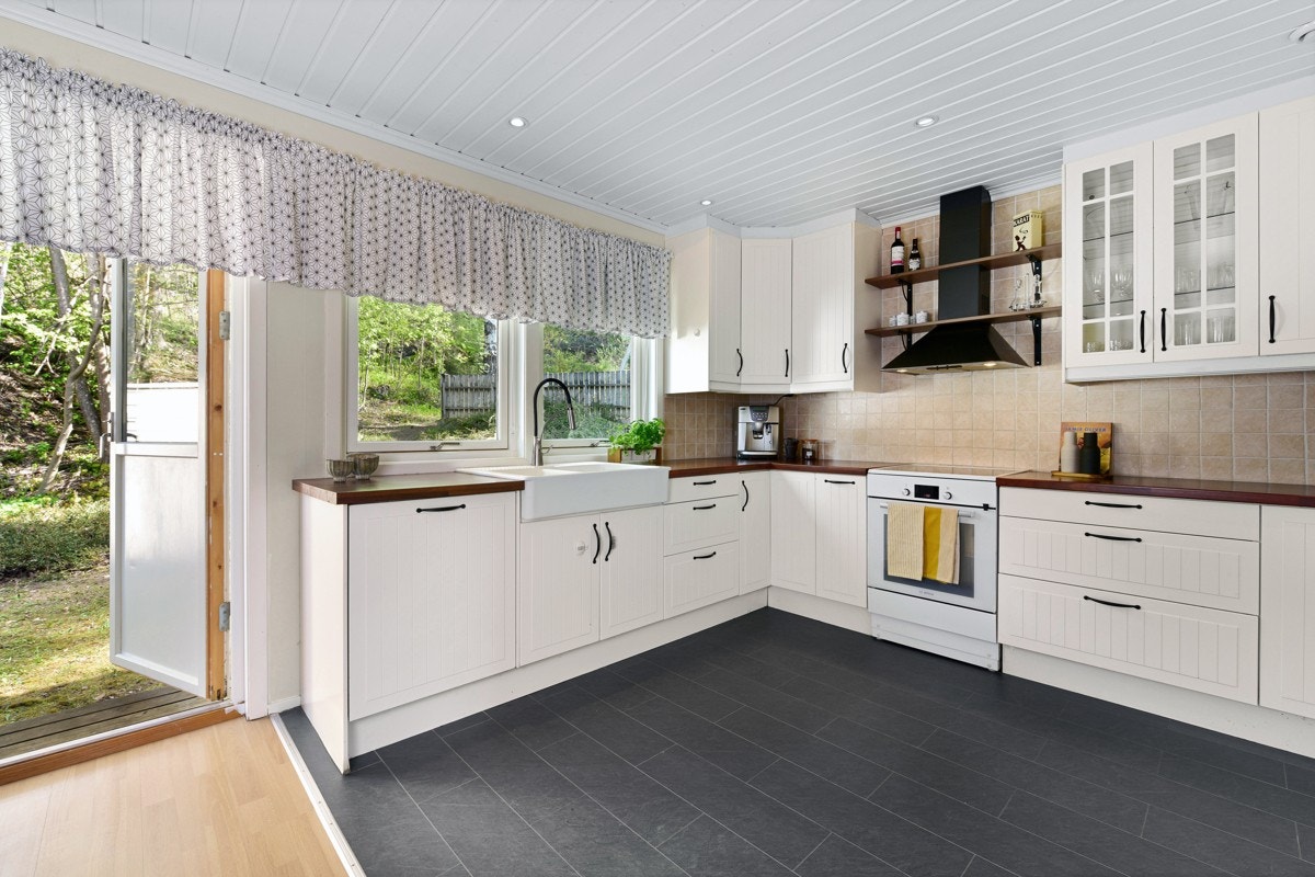 Innredningen er takhøy og har lyse, profilerte fronter, vitrineskap, beige fliser over benk og laminerte benkeplater med stor porselenskum. Galleribilde