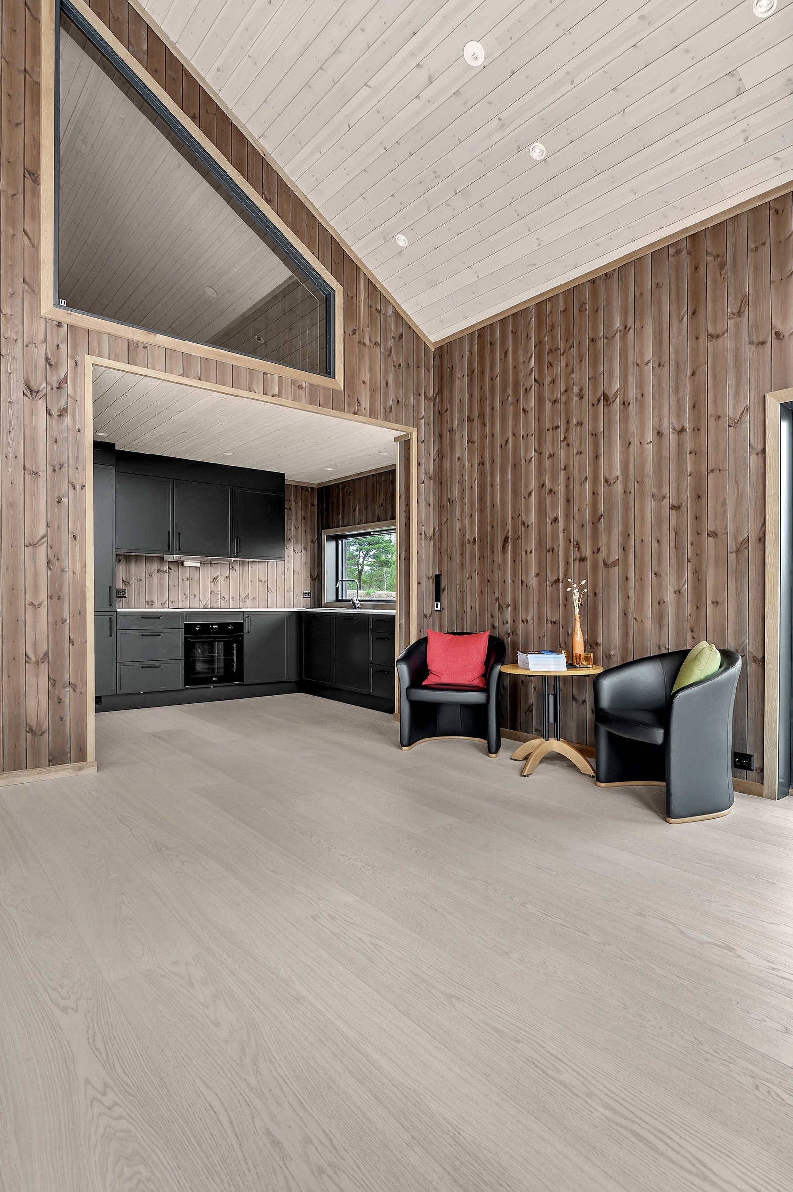 Hytta har åpen himling i stua. Her ser man et stort vindu på Hemsen. Galleribilde