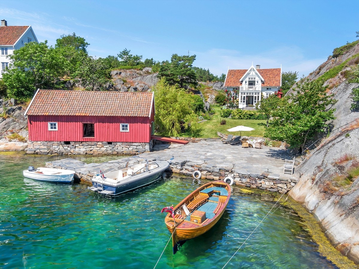 Stort bryggeanlegg med plass til flere båter, stor sjøbu over to etasjer og huset innenfor Galleribilde