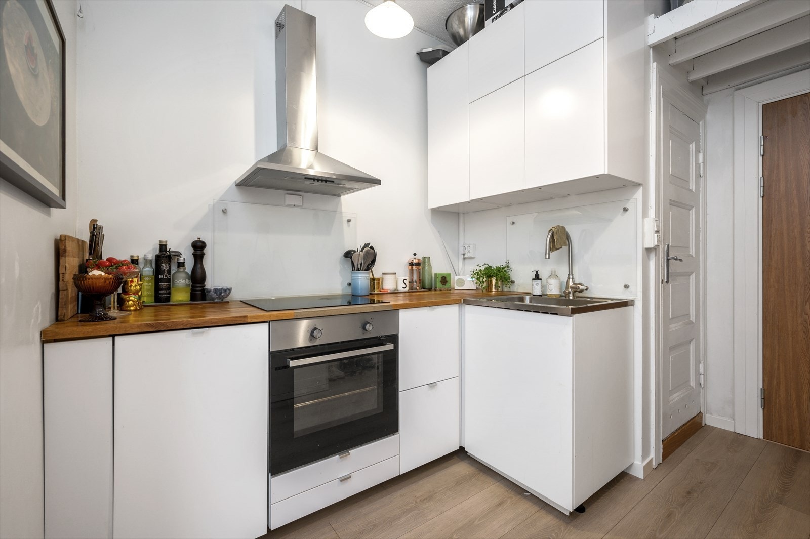 Kjøkkeninnredning med glatte fronter, glassplater på vegg over kum og stekeovn, heltre benkeplate, benkebeslag i rustfritt stål med kum kullfilterventilator, induksjonstopp, stekeovn, oppvaskmaskin er integrert i innredningen og komfyrvakt. Galleribilde