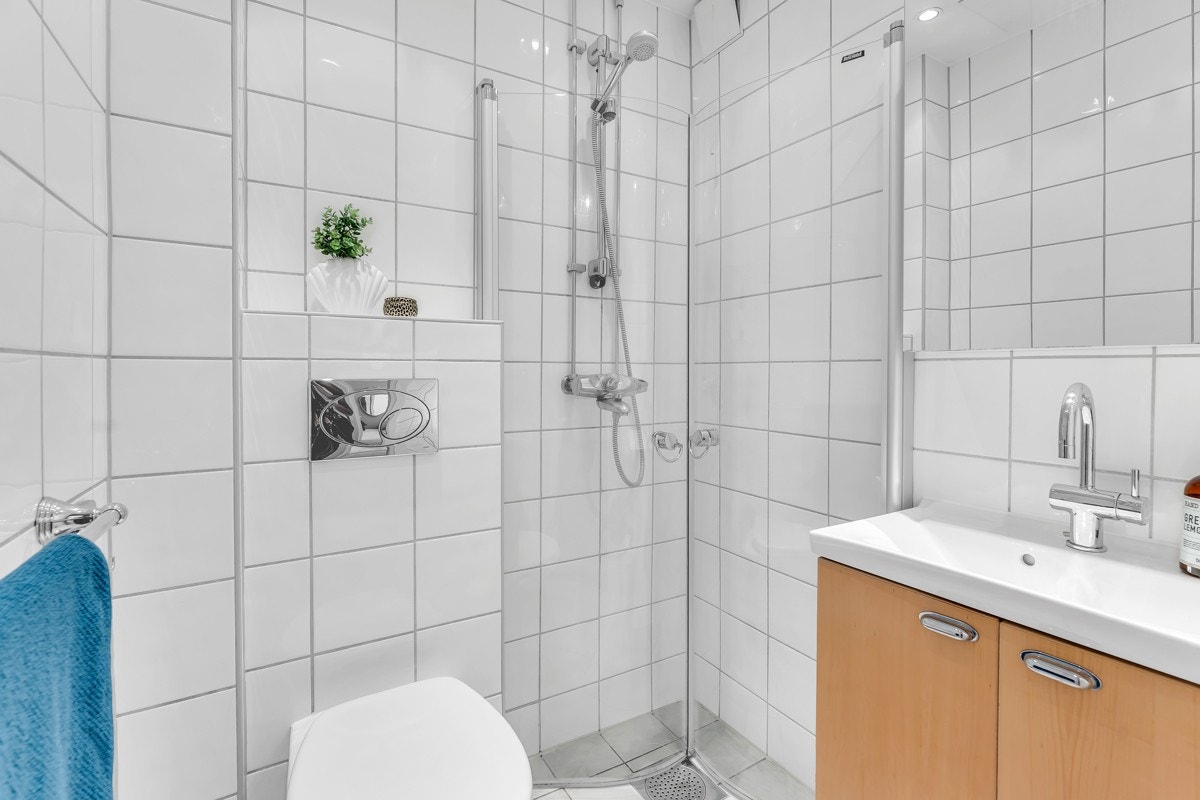 Lyst flislagt bad som er utstyrt med servant og ett-greps blandebatteri, speilskap, lys, dusjhjørne med glassdører og vegghengt toalett. Badet er fra 05/06 og ble utført i regi av aksjeselskapet. Galleribilde