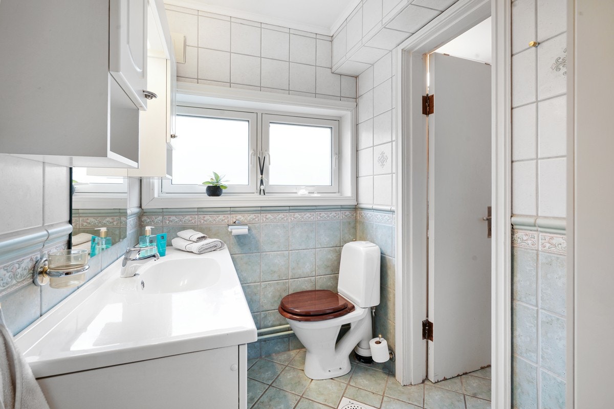 Andre del av badet har toalett, samt hvit innredning med profilerte fronter, heldekkende servant og to veggskap. Galleribilde