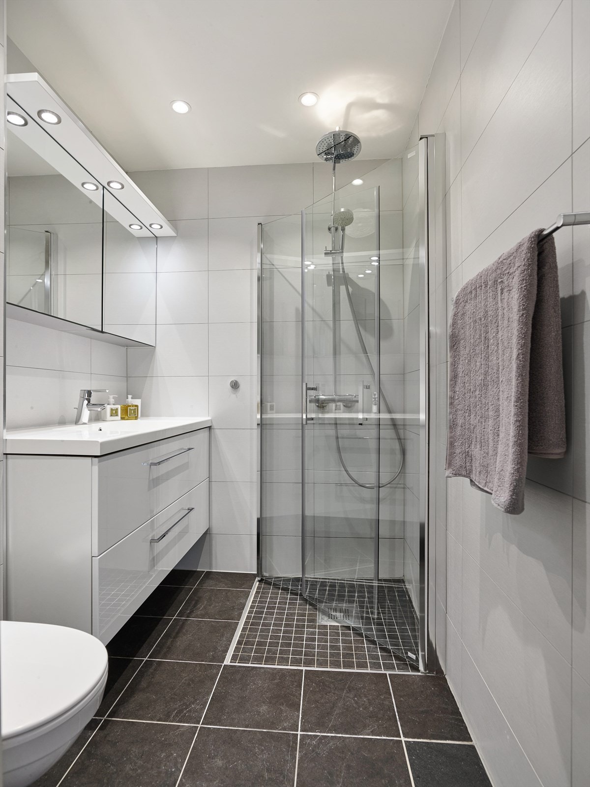 Bad innredet med veggmontert toalett, heldekkende servant m/skuffeseksjon og dusjhjørne m/ Innfellbare vegger. Galleribilde