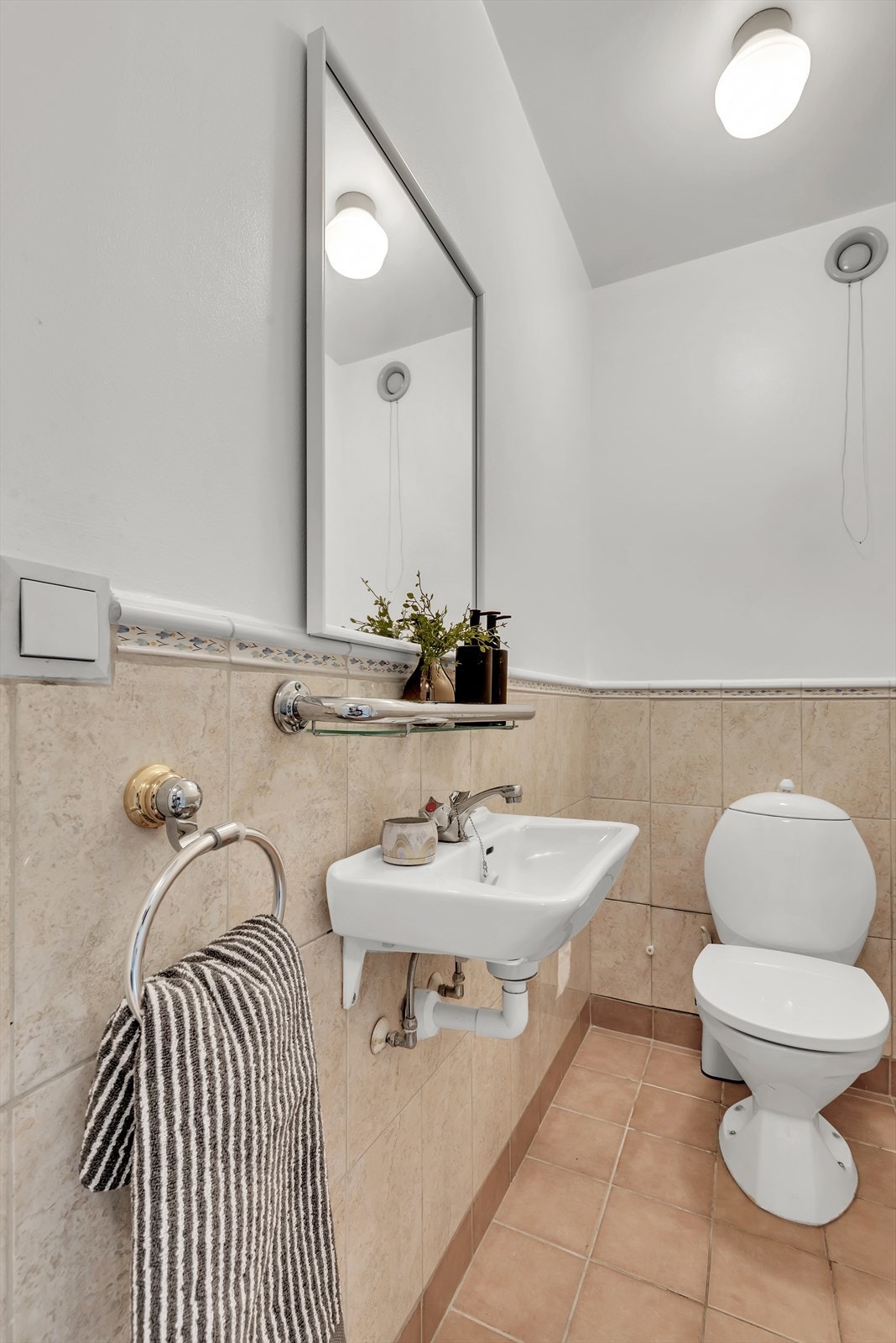 Vegg i vegg med leilighetens bad er det et toalettrom med flislagt gulv bestående av klosett, servant og speil. Galleribilde