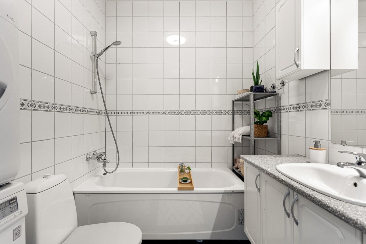 God oppbevaringsplass i baderomsinnredning med lyse profilerte fronter og laminert benkeplate med nedfelt servant, ekstra vegghengte skap og speil med belysning over. Galleribilde