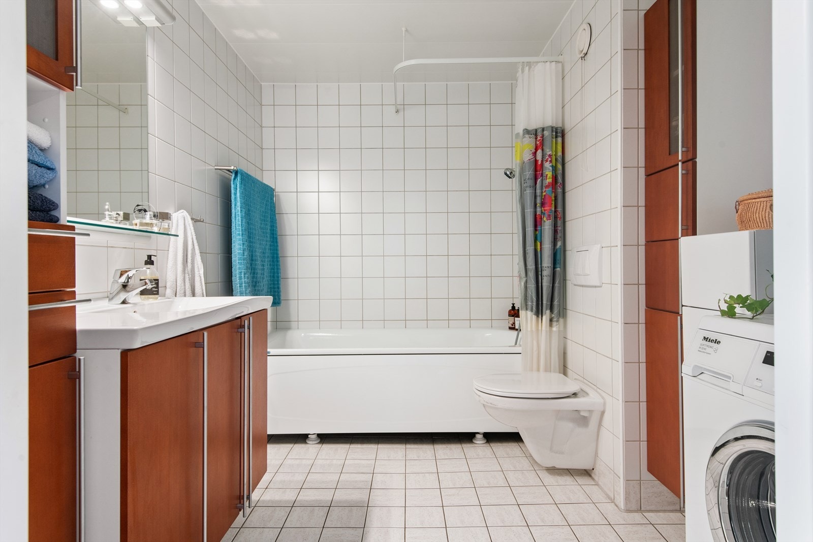 Badets vegger og gulv er flislagt i lyse toner. Det har varme i gulv og er ellers utstyrt med vegghengt toalett, badekar med dusjarmatur og opplegg til vaskemaskin. Galleribilde