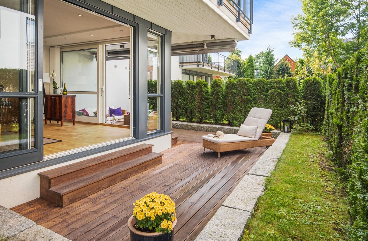 Terrasse med terrassebord som ble lagt for ca. 5 år siden, og er avgrenset med kantstein i granitt, og tujahekk Galleribilde