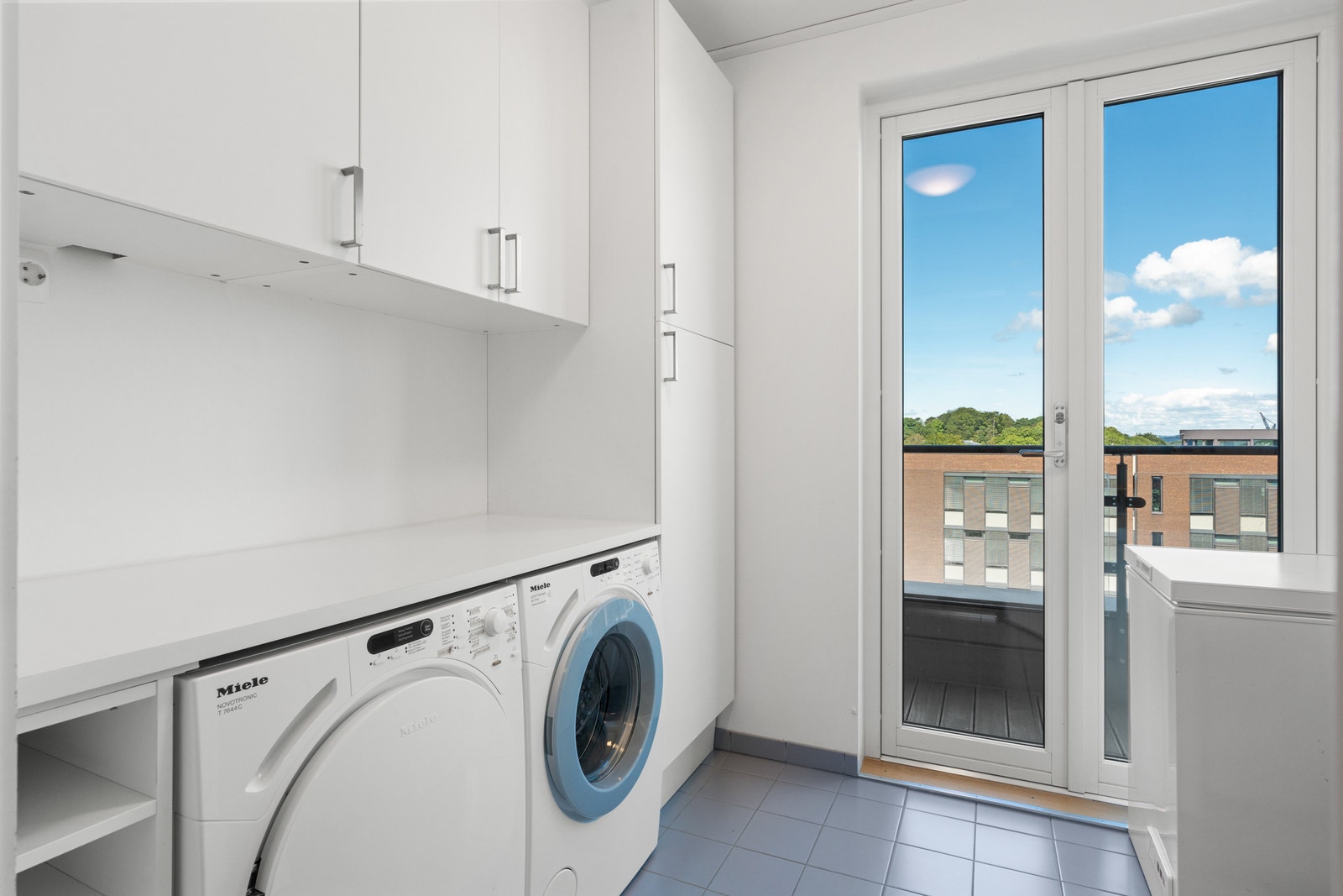 Laundry room with ensuite balcony, including washing machine, dryer, sink, extra freezer, fridge and storage space. Galleribilde