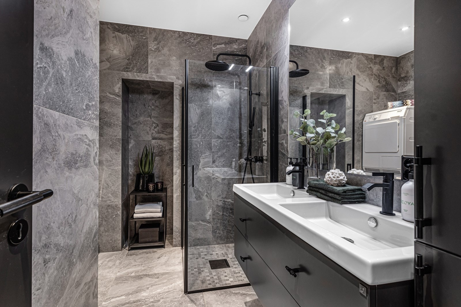 Rålekkert og moderne bad fra 2019/2020 bestående av vegghengt toalett, servantinnredning med dobbelvask, speil og lys på vegg samt dusj på gulv med glassdører Galleribilde