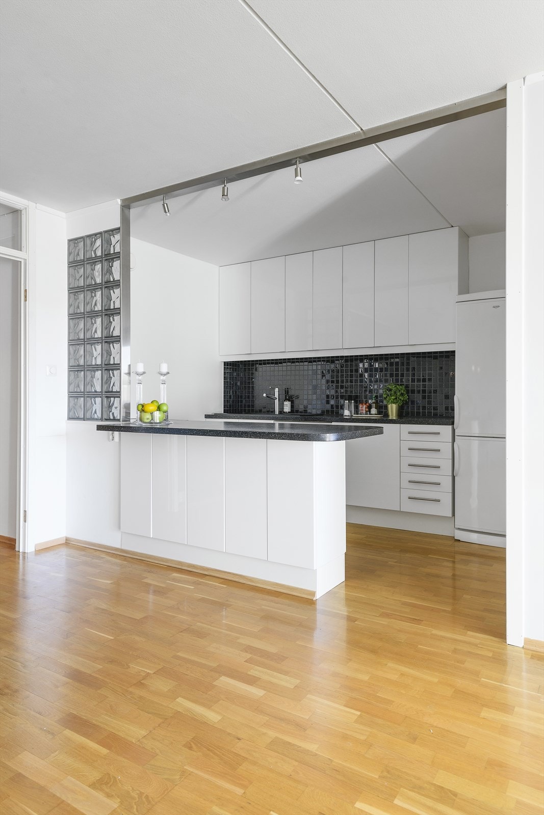 Kjøkkenet i leiligheten gir et moderne uttrykk med hvite glatte fronter, takhøye overskap og en halvøy mot stuen for ekstra benkeplass Galleribilde