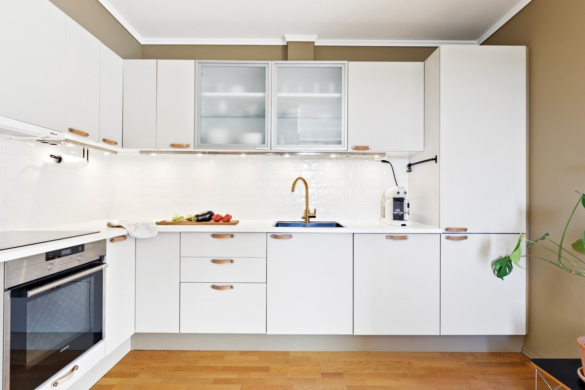 Slette, sandfargede fronter og hvit laminat benkeplate, nedfelt sort oppvaskkum med et kontrastgivende ettgreps blandebatteri i rustfritt stål (Primy). Galleribilde