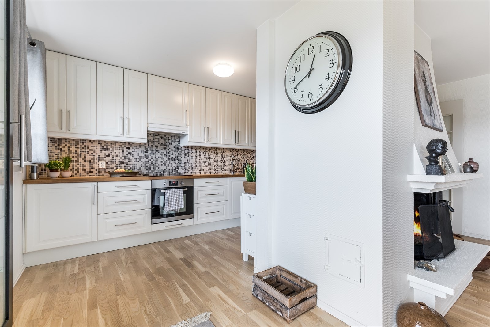 Pen kjøkkeninnredning med med hvite profilerte fronter, fliser over heltre benk og dobbel stålkum med ett-greps blandebatteri. Galleribilde