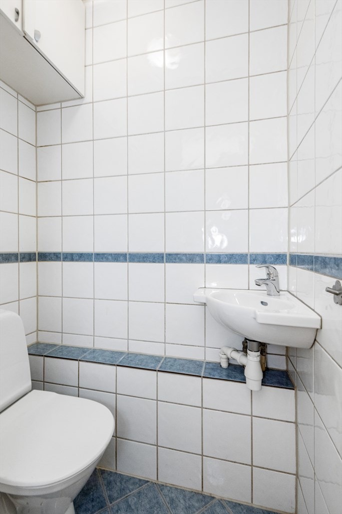 Vegg-i-vegg med badet ligger et toalettrom med blå gulvfliser, lyse veggfliser, servant og toalett. Galleribilde