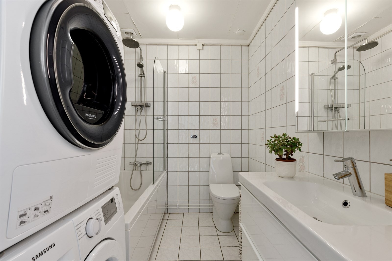 Fliselagt baderom med badekar, nyere baderomsinnredning og opplegg for vaskemaskin Galleribilde