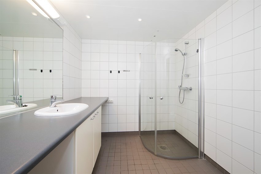 Badet fremstår som romslig og pent, med hvite fliser på veggene, downlights i himlingen og grå fliser på gulv med gulvvarme. Galleribilde