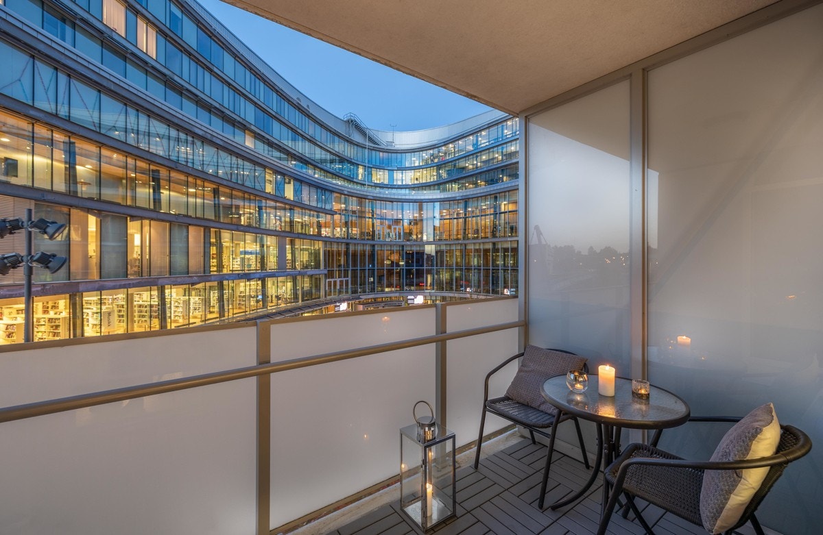 Utgang fra stue til balkong som vender inn mot indre torg og Lørenskog Hus. Boligen har en nordøstvendt balkong på ca. 5 kvm med tremmefliser på dekke og utestikk. Galleribilde