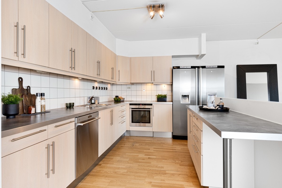 Pen kjøkkeninnredning med god benke- og lagringsplass. Innredningen er fra HTH og har lyse, glatte fronter og benkeplate i laminat med planlimt vaskekum i rustfritt stål Galleribilde