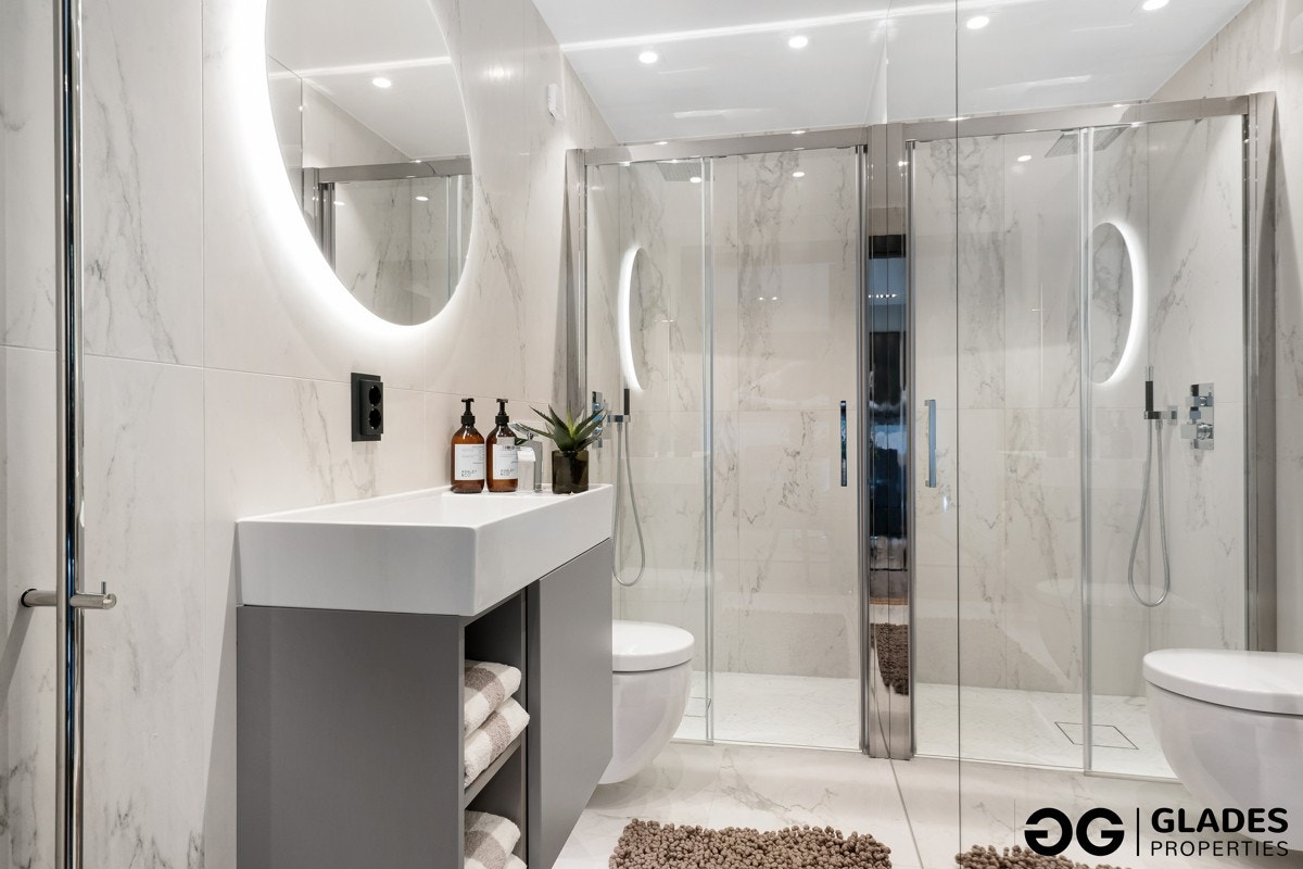 Badet er utstyrt med vegghengt toalett, dusjnisje med skyvedør og integrert dusjbatteri med hånddusj. Det er veggmontert håndvask med skap og et rundt speil med lys. Håndkletørker INR Line. Galleribilde