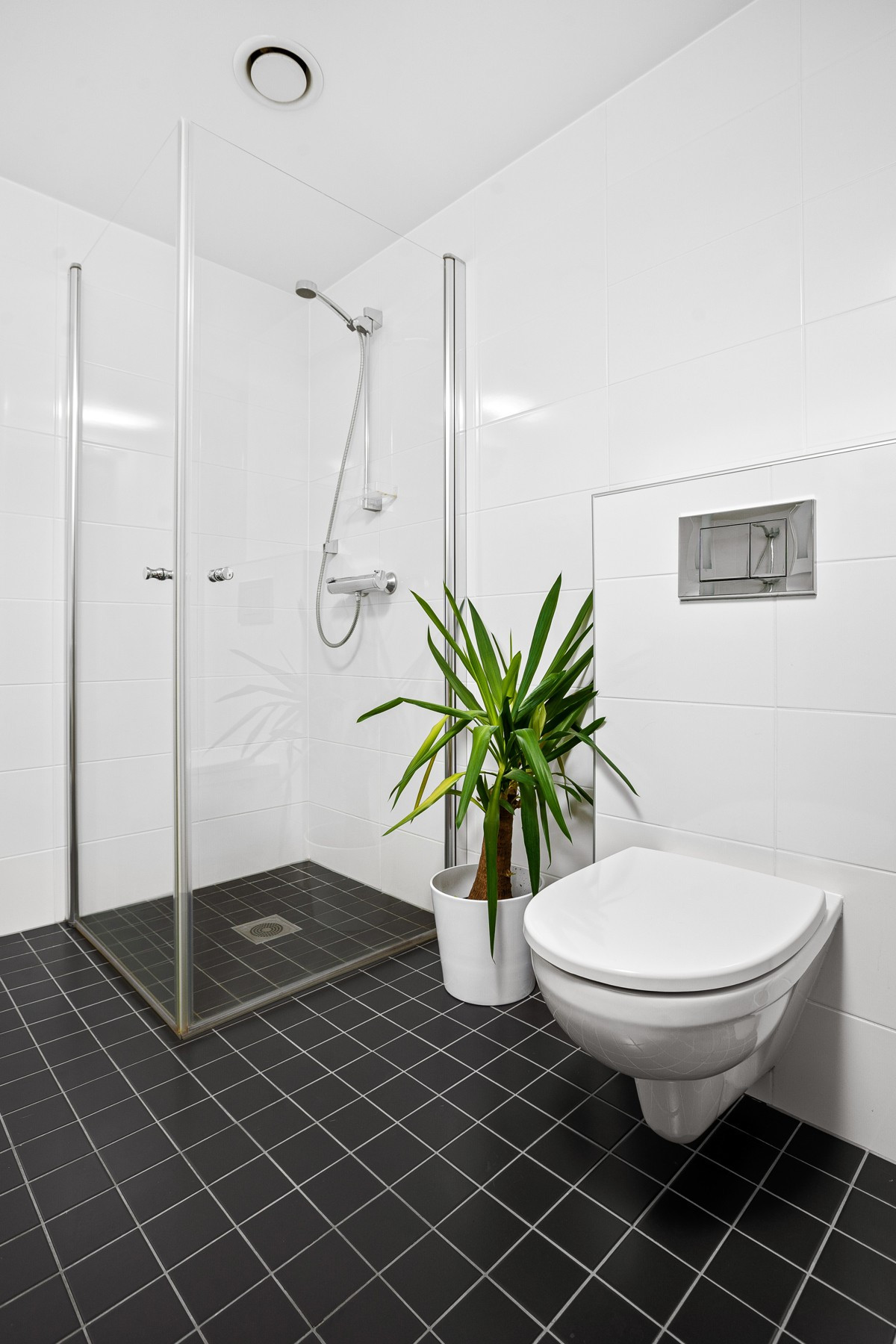 Badet er komplett flislagt med vegghengt toalett, dusjhjørne og servant med speil