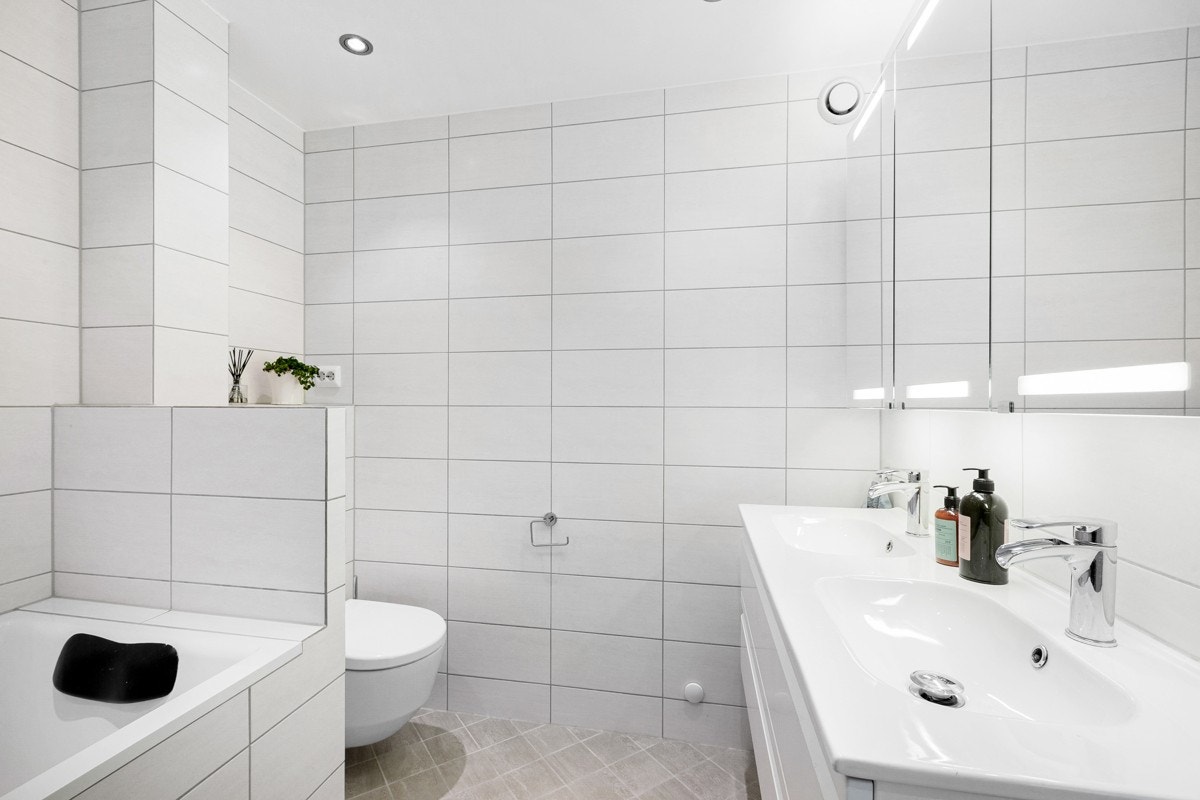 Den hvite baderomsinnredningen har heldekkende dobbelservant og stort speilskap med integrert belysning. Galleribilde