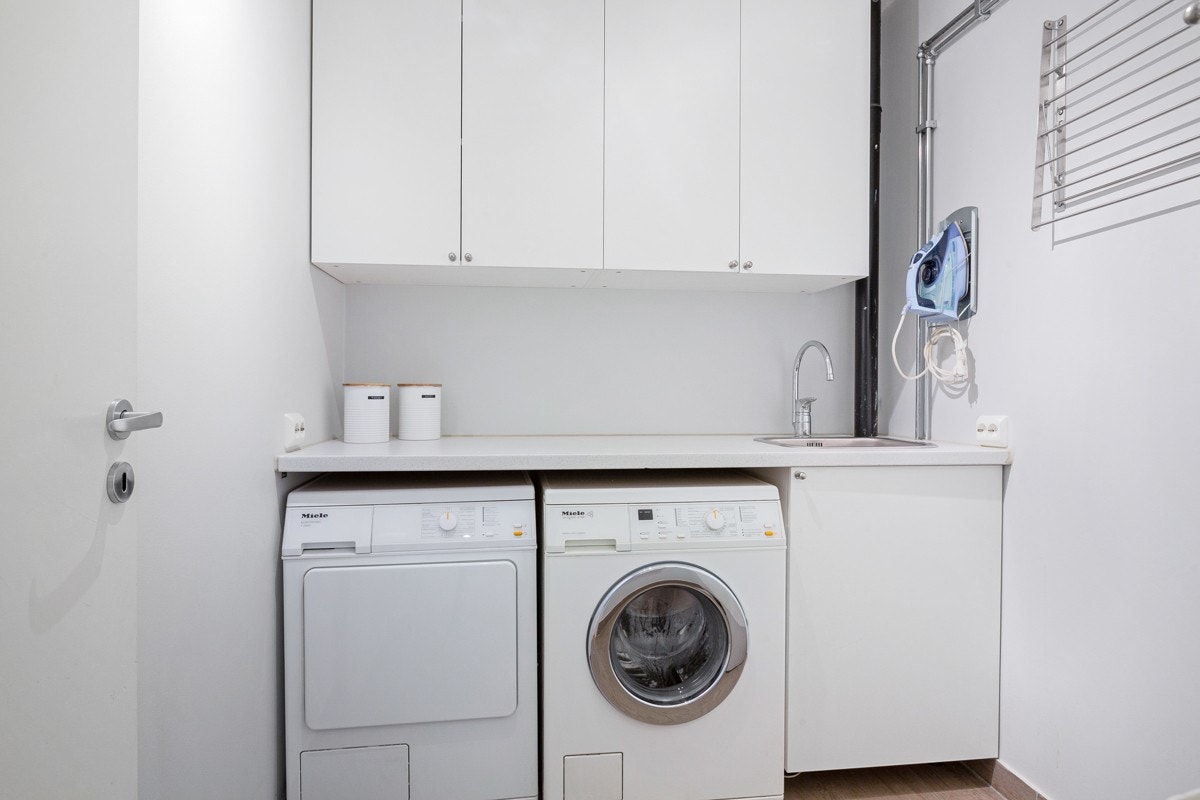 Leiligheten har separat vaskerom med hvit innredning og plass til både vaskemaskin og tørketrommel under benken. Galleribilde