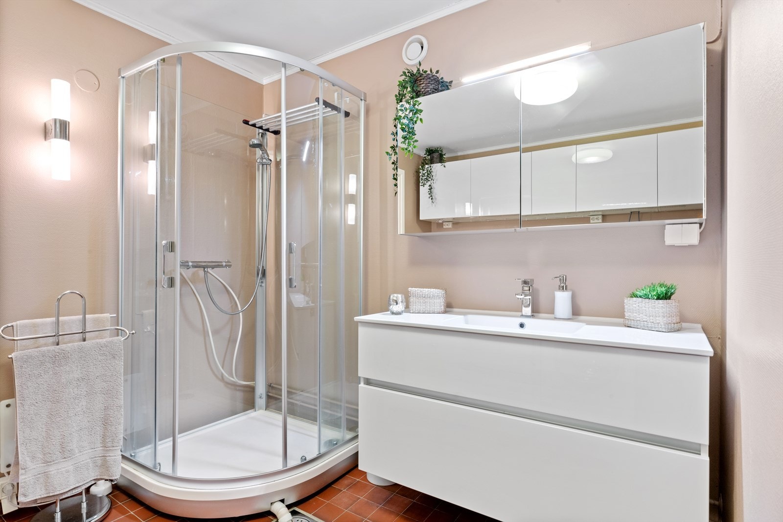 Badet er innredet med baderomsmøbel med servant og ett-greps blandebatteri, speilskap med overlys, dusjkabinett, overskap for oppbevaring og veggmontert skyllekum med veggmontert ettgreps blandebatteri. Galleribilde