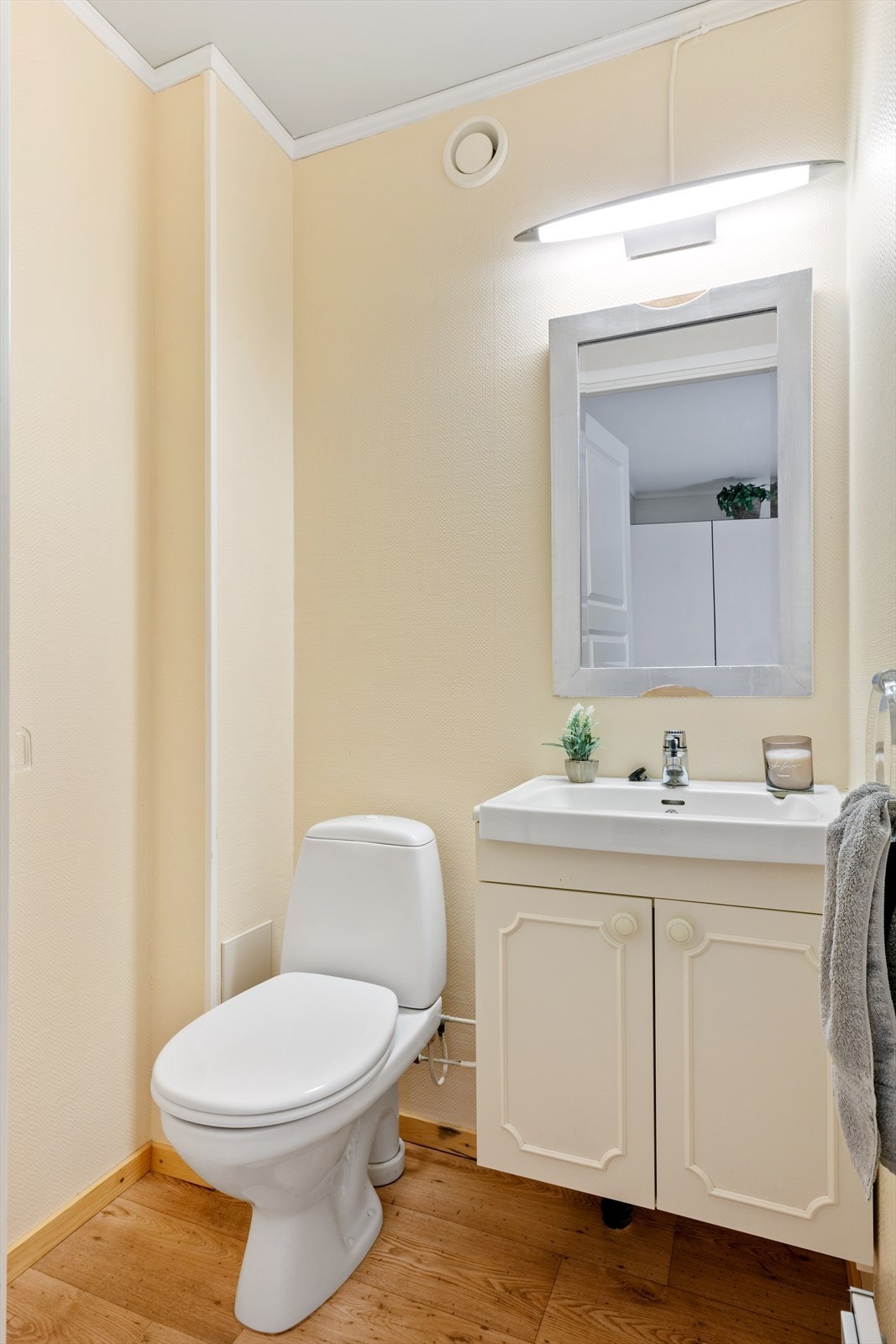 Wc er innredet med gulvstående toalett, servant med underskap og speil. Det er montert lys over speil. Galleribilde