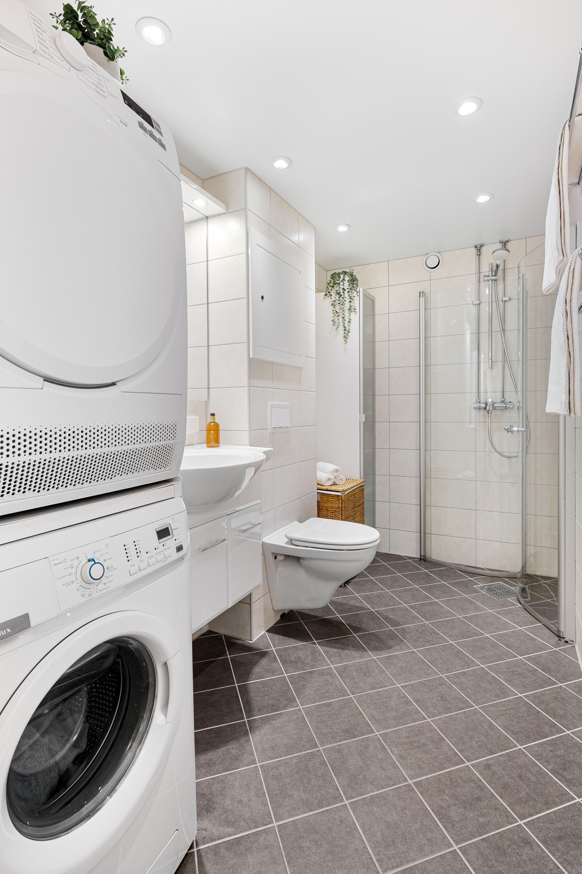 Praktisk dusjhjørne med buede svingdører av herdet glass, vaskesøyle med opplegg til vaskemaskin og tørketrommel Galleribilde