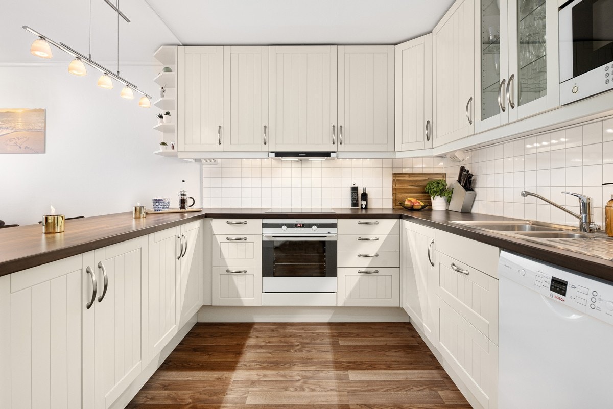 Åpen kjøkkenløsning, takhøy innredning. Profilerte, sprøytelakkerte fronter, laminat benkeplate med nedfelt kum i rustfritt stål. Galleribilde