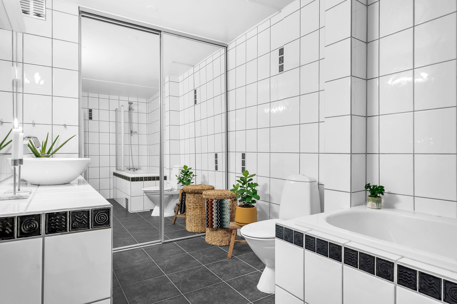 Badet er av generøs størrelse. Rommet består av opplegg til vaskemaskin, gulvmontert toalett, innbygget badekar med dusjvegger i glass og servantinnredning Galleribilde