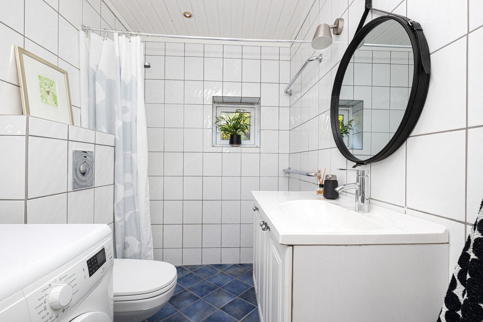 Flislagt bad med vegghengt toalett, servant, dusj og uttak til vaskemaskin. Galleribilde