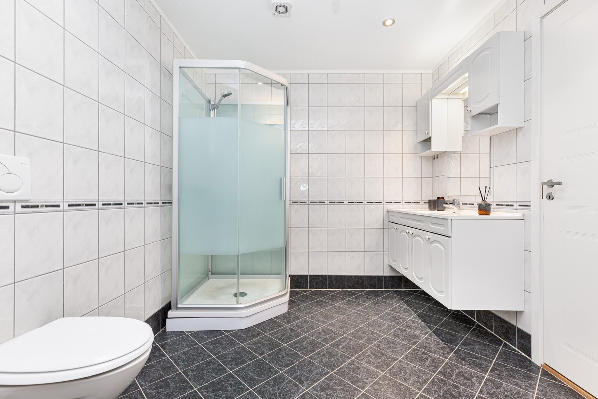 Stort fliselagt baderom med dusjkabinett, wc og servant