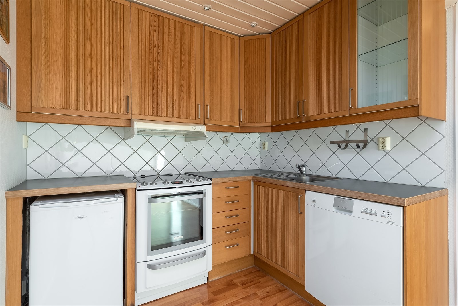 Kjøkkenet er utstyrt med hvitevarer som komfyr med keramisk topp, oppvaskmaskin (defekt), lite kjøleskap under benk samt ventilator (dekfekt) over kokesone. Galleribilde