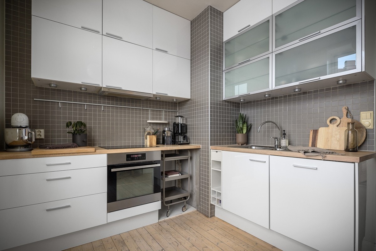 Brede benkeplater i heltre med to stålkummer og ettgreps blandebatteri. Dekorative fliser på vegg over benken og montert lekkasjestopper i underskapet. Galleribilde