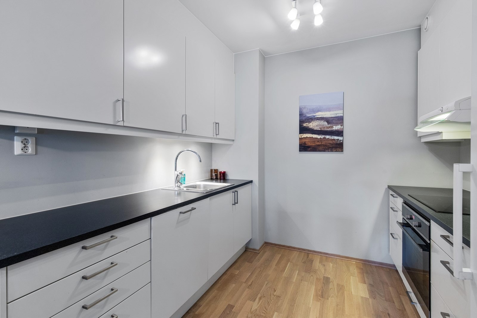 Kjøkkenet har en lys og tidløs innredning med hvite glatte fronter, sort benkeplate og intergrerte hvitevarer (uten fryser). Galleribilde