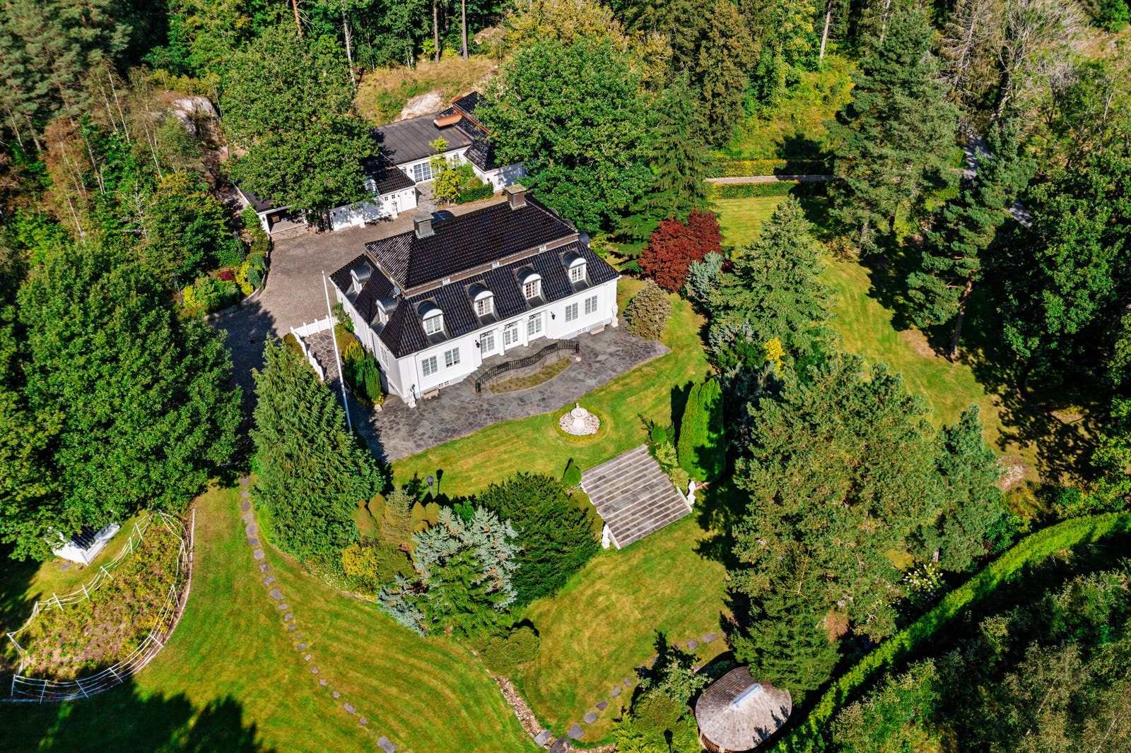 Dronefoto over del av eiendommen med hovedhuset i midten Galleribilde