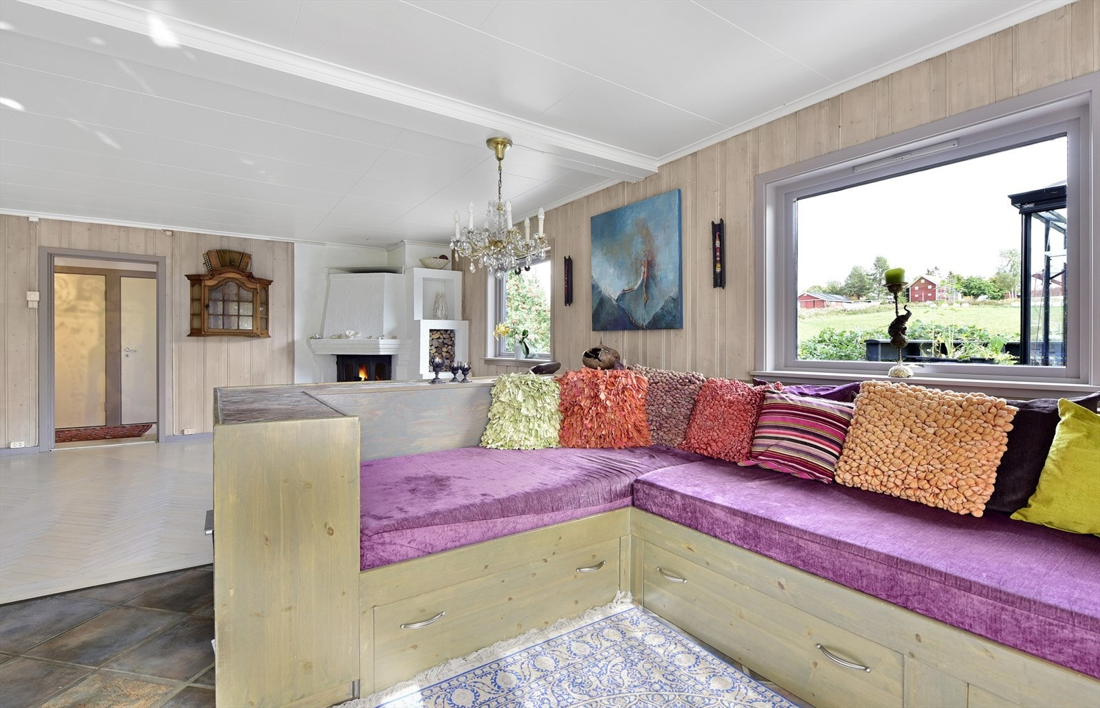 Stuedelen i allrommet i hovedhuset har fliser på gulvet, peis og panelvegger. Den plassbygde vinkelsofaen har også rom til oppbevaring. Galleribilde