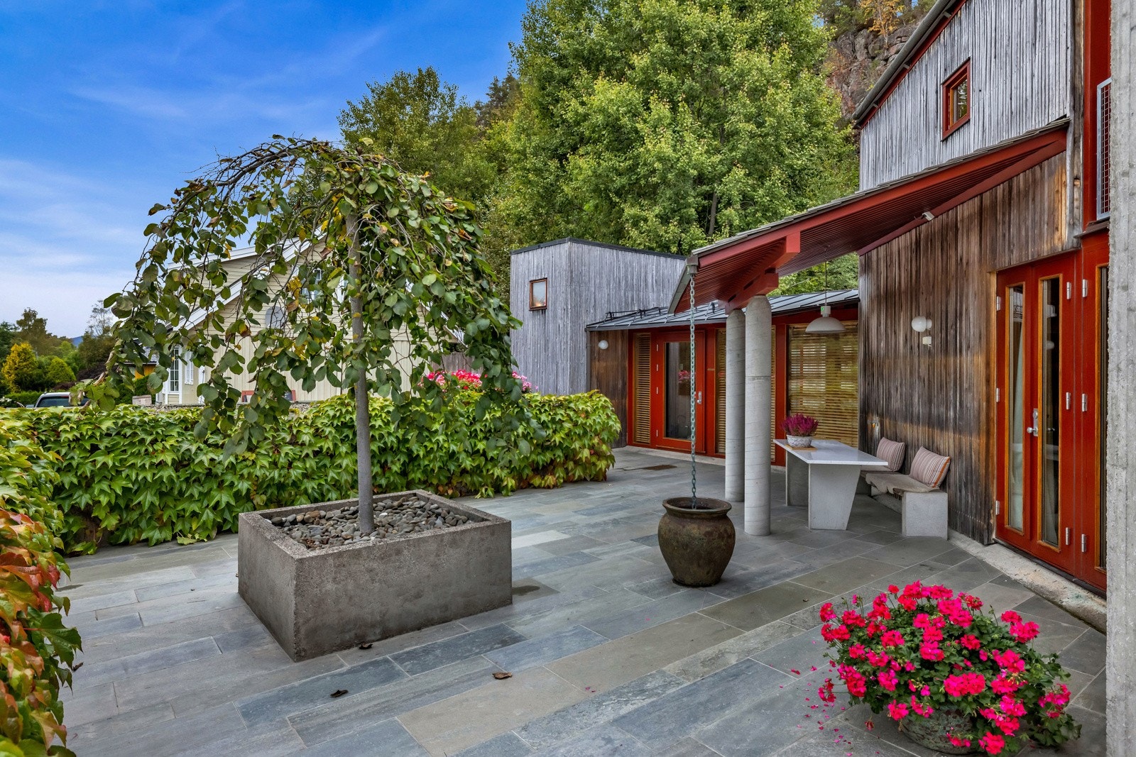 Terrassen mot vest er skiferbelagt med beplantning langs muren mot veien som bidrar med det lille ekstra til stemningen og estetikken hvor man kun ser åsene rundt. Galleribilde