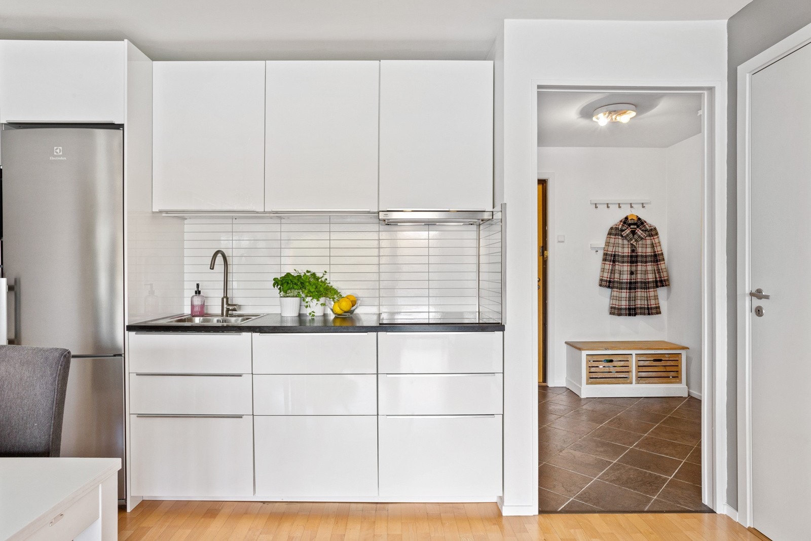 Hvite glatte fronter og benkeplate av laminat. Kjøkkenet er utstyrt med integrert oppvaskmaskin, induksjon koketopp, komfyr og mikro fra Ikea montert i høyskap. Plass til kjøleskap med frysedel. Galleribilde