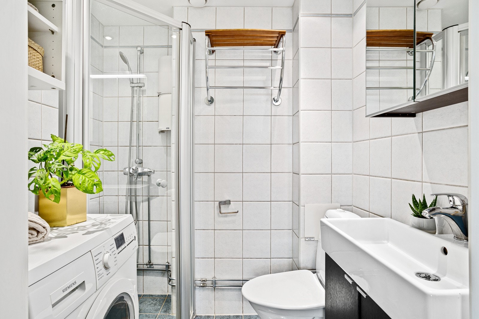 Praktisk baderom med gulvvarme og opplegg for vaskemaskin. Tidløse flisvalg med gulvfliser i grånyanser og veggfliser i hvitt. Galleribilde