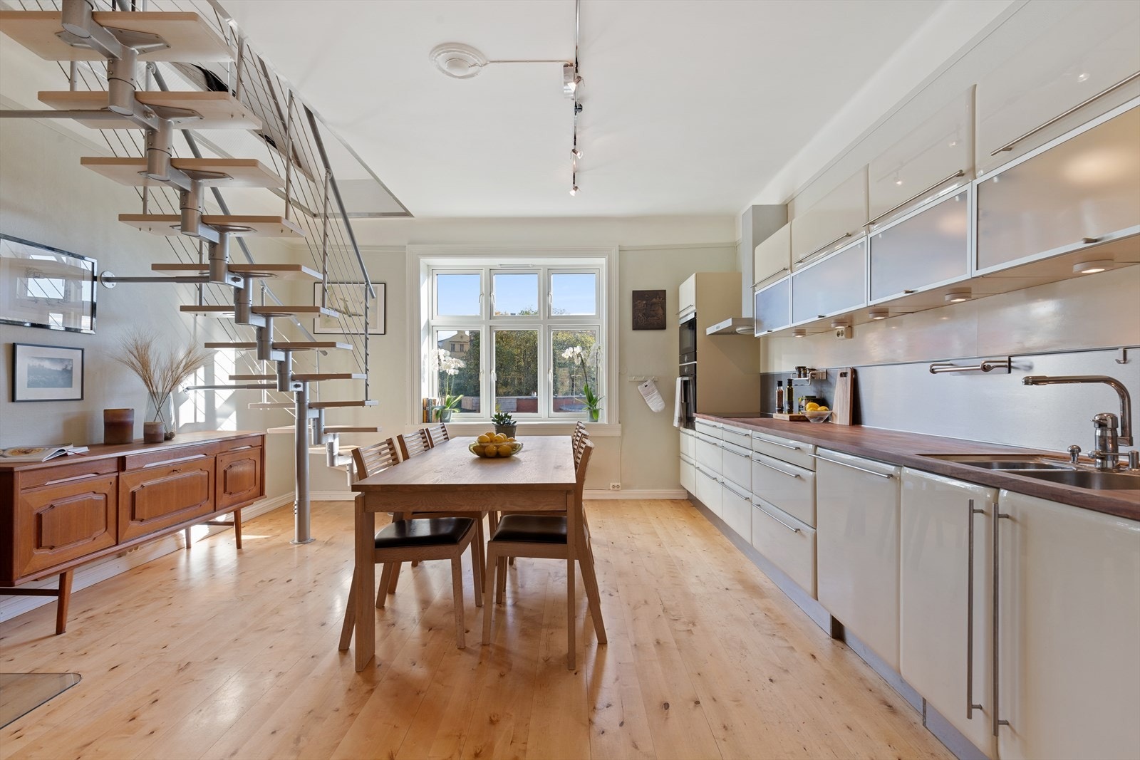 Kjøkkeninnredningen har lyse matte fronter, flere overskap med fronter i glass og benkeplate i heltre med underlimt oppvaskkum. Galleribilde