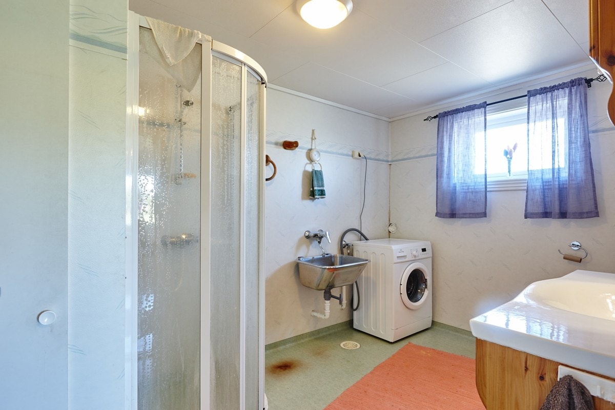 Innredning med fronter i tre med nedfelt servant med skap under, skap med speil og lyslist over, dusjhjørne, toalett og opplegg for vaskemaskin. Galleribilde