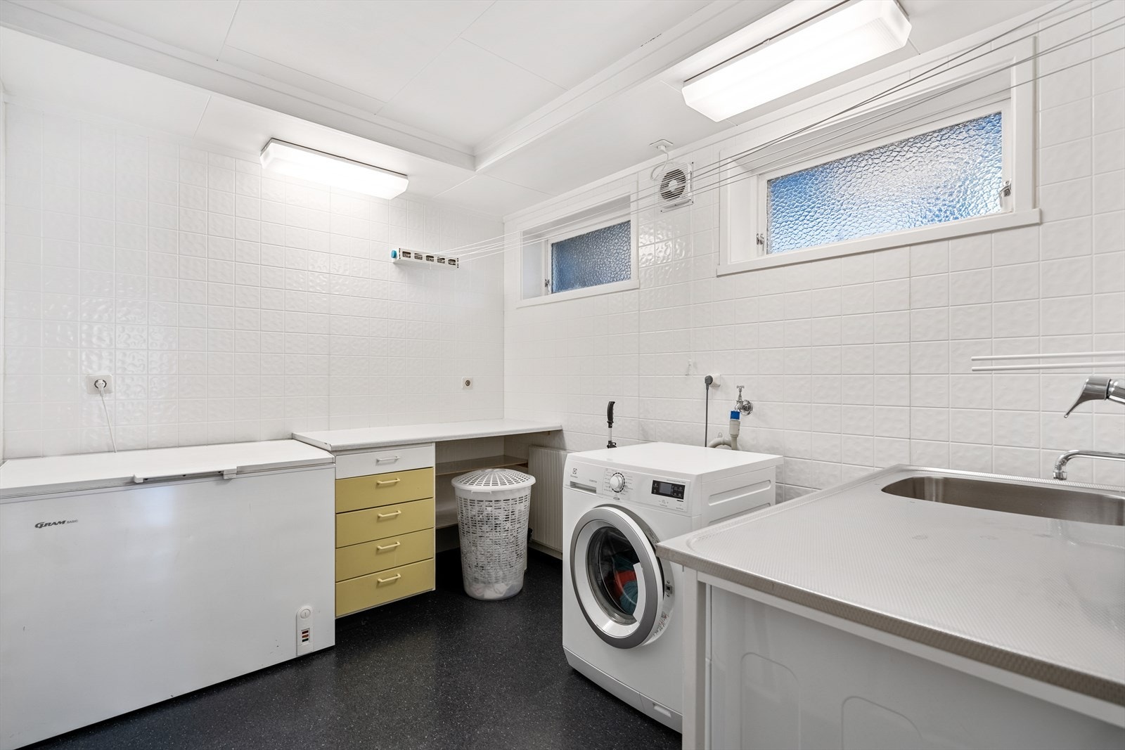 Vaskerom i underetasjen med stålbenk og skyllekar. Oppbevaring i skap med skyvedører. Galleribilde