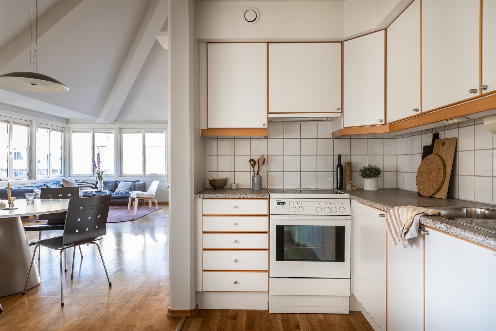 Det er takhøy kjøkkeninnredning fra byggeår med glatte malte fronter med tre kant lister, laminat benkeplate med nedfelt rustfri kum og nisjer for hvitevarer. Galleribilde