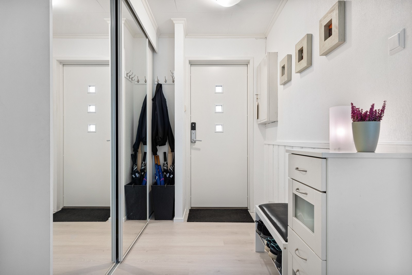 Vel innenfor en ytterdør med glassfelt og kodelås er det en pent innredet entré. Entreen har hvitmalte vegger over hvitmalt brystningspanel, et tidsmessig Pergo laminatgulv som var nytt i 2021 og skyvedørsgarderobe med speilfronter. Galleribilde
