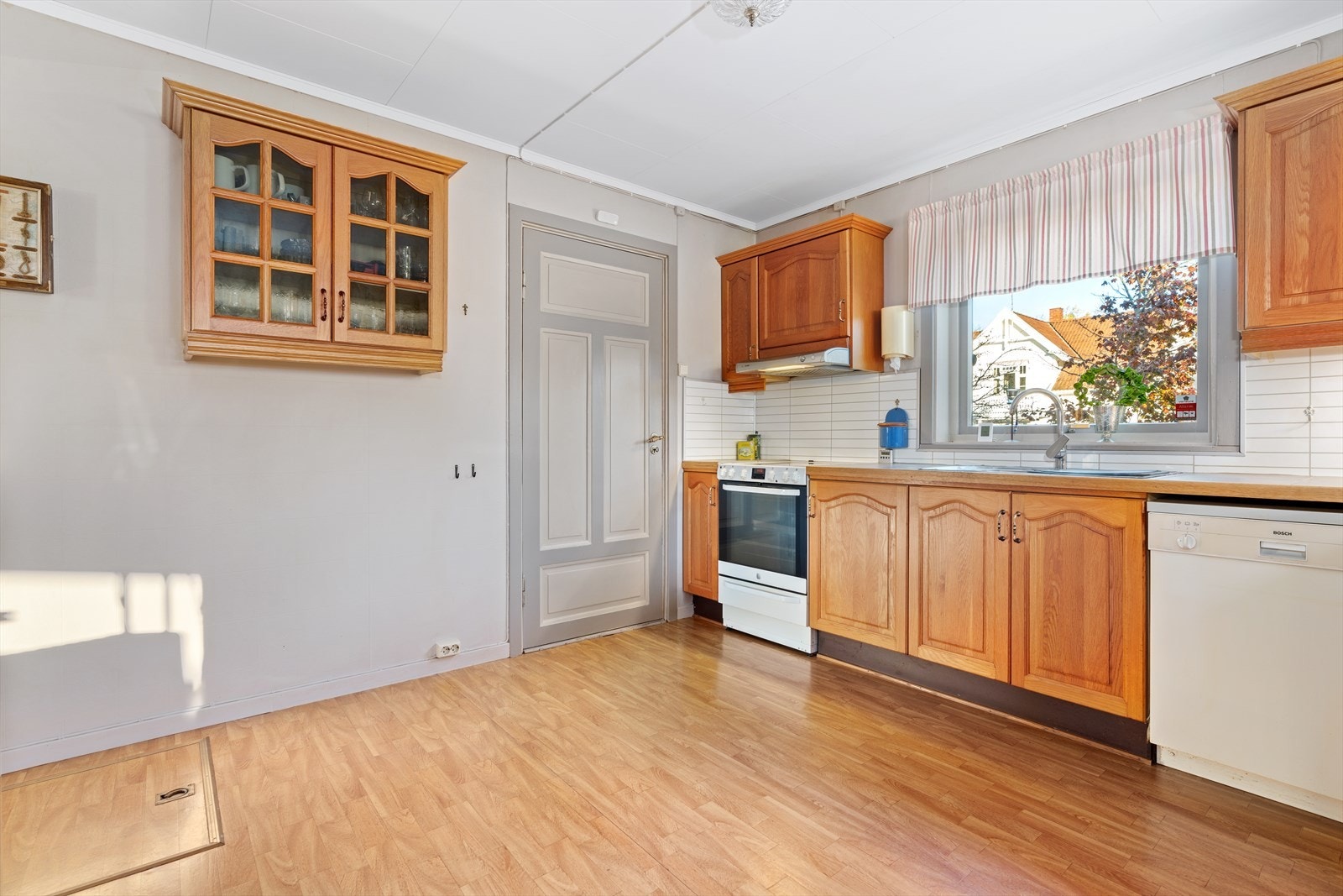 Eldre kjøkkeninnredning med profilerte eikefronter, ventilator over kokesone, plater over benk og belysning under overskap. Galleribilde