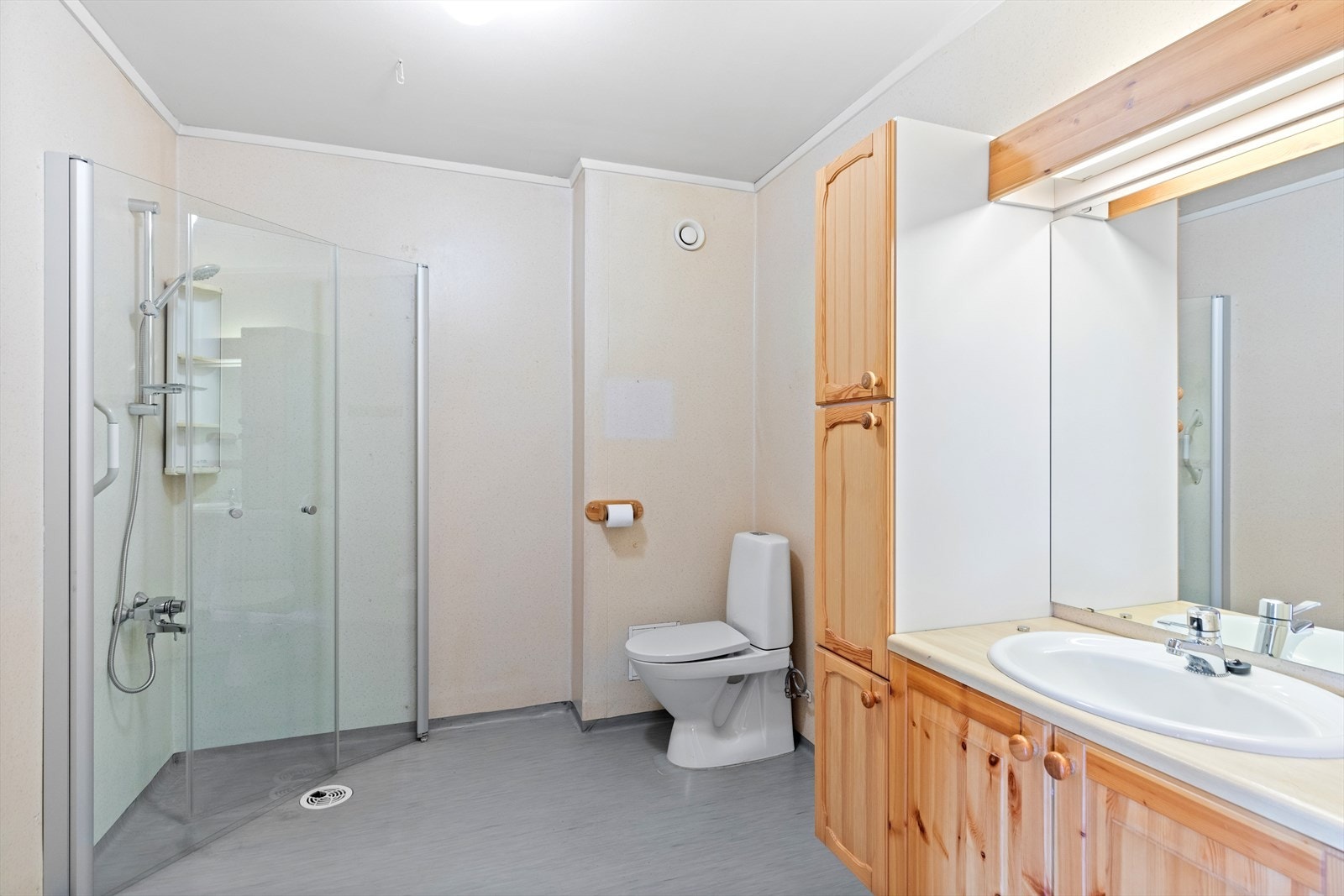 Badet er utstyrt med servantskap, veggskap, høyskap, vaskekum, gulvfestet toalett og dusjhjørne med innfellbare glassdører. Galleribilde