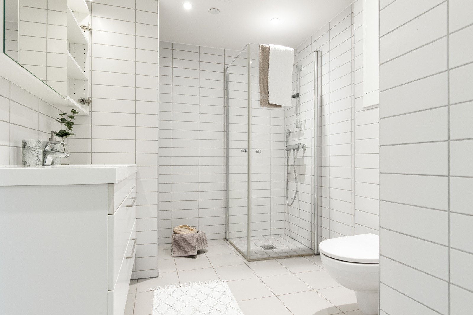 Baderommet har et stilrent uttrykk med hvite fliser i to størrelse på vegger og gulv. Galleribilde