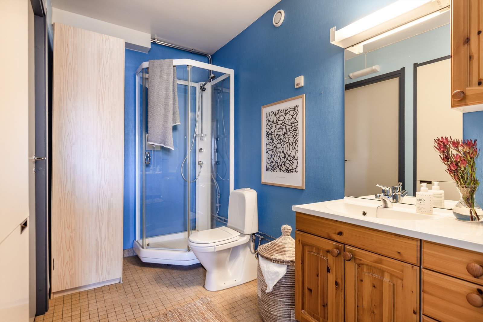 Baderom med servant, speil, klosett, dusjkabinett og opplegg til vaskemaskin. Galleribilde